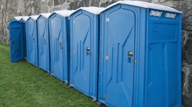 Row of blue portable toilets lined up on grass against a stone wall for event sanitation in Wichita, KS