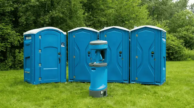 Four blue portable toilets and a matching hand washing station on grass near trees, a common sight at local outdoor events in Wichita, KS