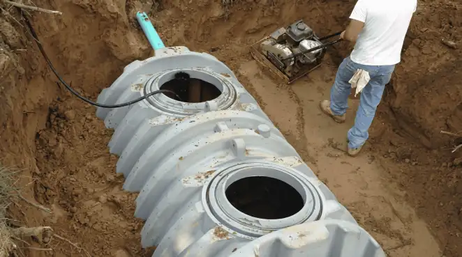 Septic tank installation showing a technician compacting soil around a new poly septic tank in an excavation pit in Wichita, KS